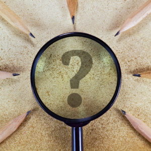 Circle of pencils pointing to a enlarged question mark under a magnify glass
