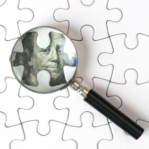 Magnifying glass uncovers money under puzzle pieces